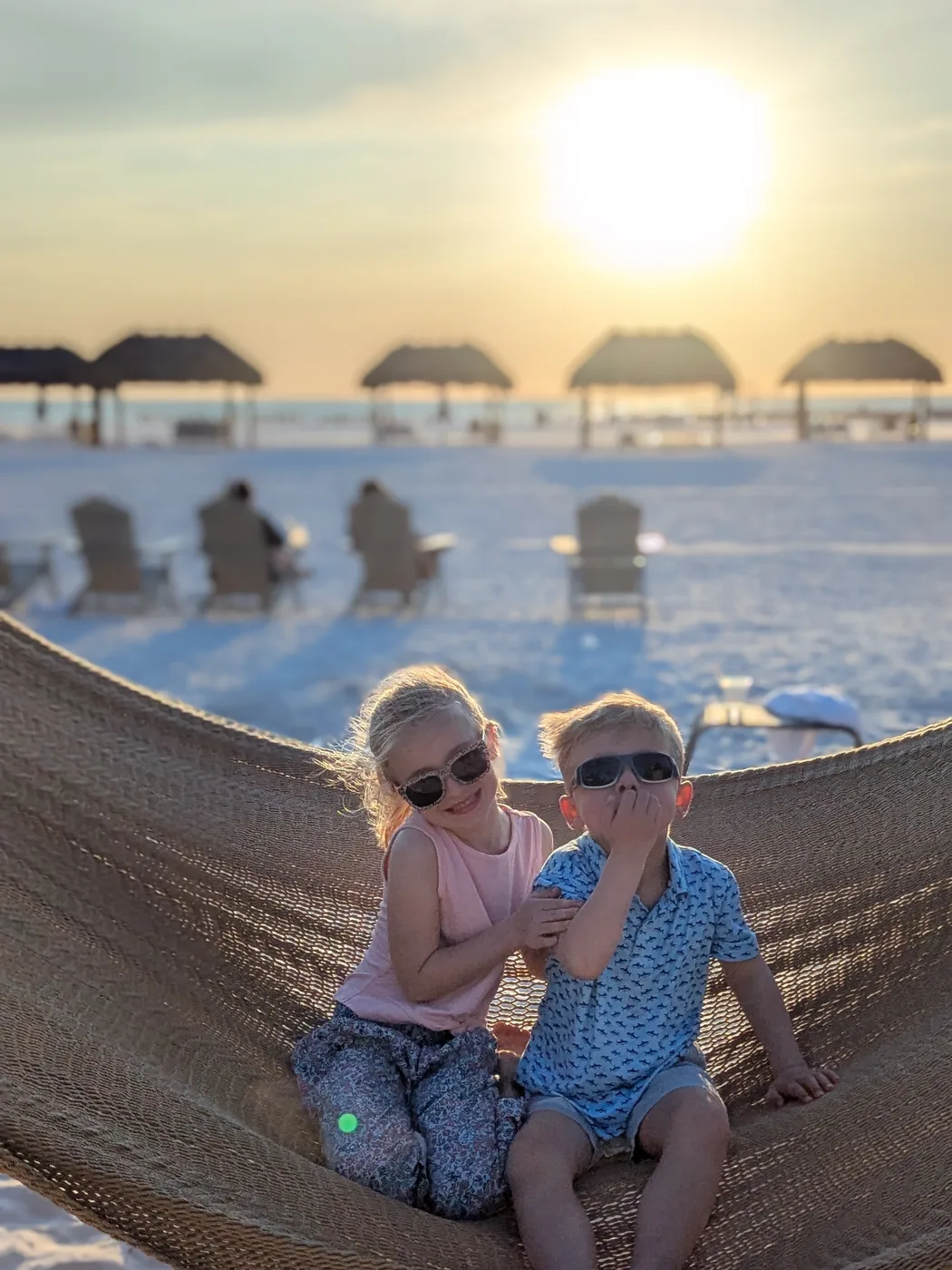 Abigail and Caleb sitting together in a hammock on the beach at sunset