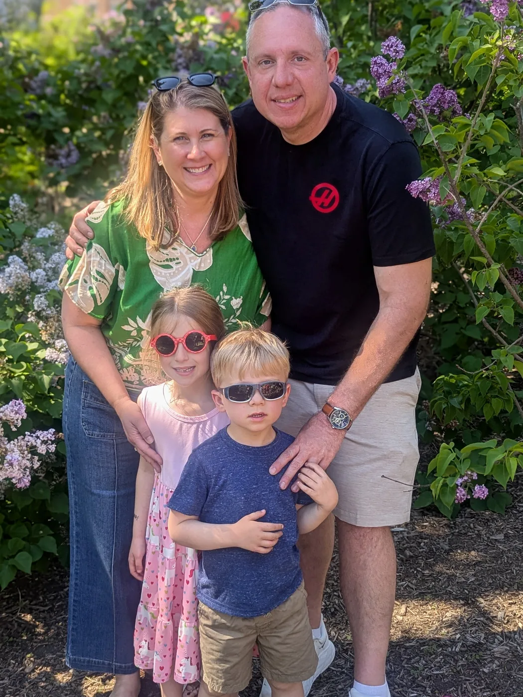 The Oswald family standing among blooming lilacs, Abigail and Caleb in sunglasses