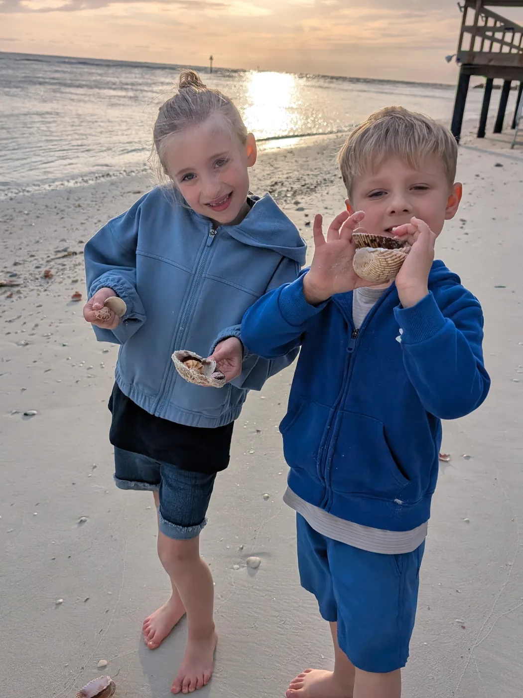 Abigail and Caleb showing off seashells on the beach at sunrise
